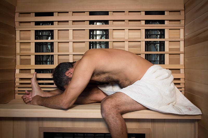 Man sitting with towel around waist getting a good leg stretch in sauna