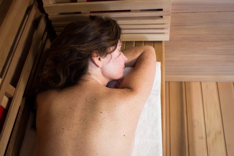 A woman laying down on a towel inside of a Health Mate infrared sauna.