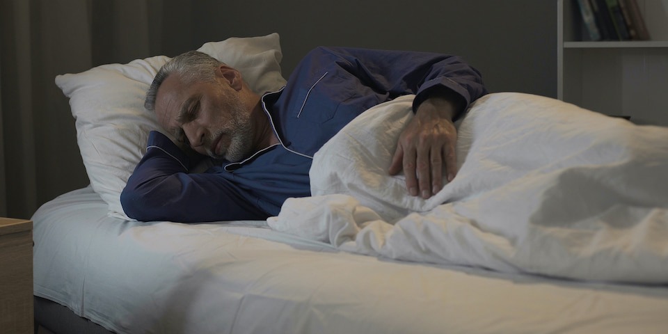 An older man sleeping on his side in bed while wearing pajamas.