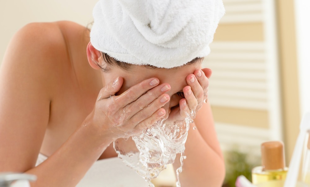 A woman wearing a robe in her bathroom splashing water onto her face.