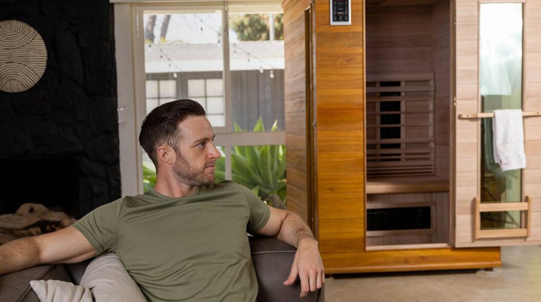 Man relaxing on couch with Enrich infrared sauna in the background