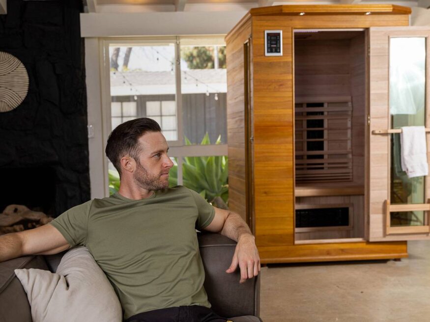 Man relaxing on couch with Enrich infrared sauna in the background