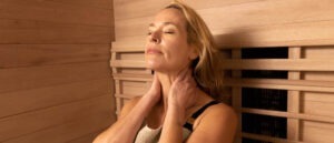 Woman sitting in infrared sauna holding her neck and relaxing