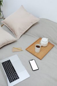 Laptop and phone on bed next to tray of coffee